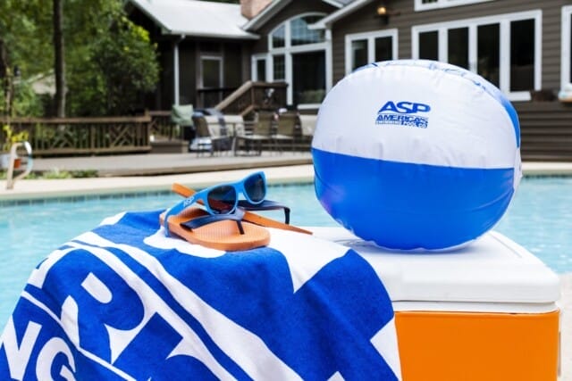 A beach ball, sunglasses, and a towel by a pool maintained by America's Swimming Pool Co., suggesting summer leisure time.