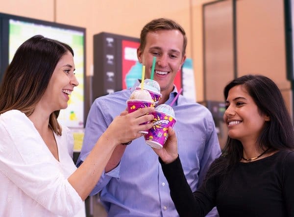 Three coworkers enjoying a light-hearted moment with a toast of 7-Eleven franchise's frozen yogurt cups.