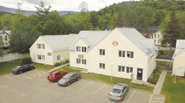 Aerial view of the Discovery Map International headquarters building, surrounded by parked cars and green hills in the background.
