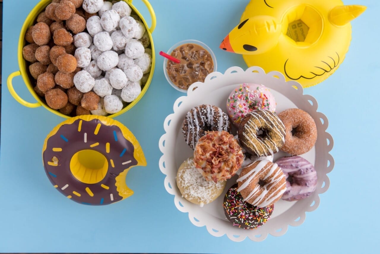 Assorted Duck Donuts on a plate and a rubber duck on a blue background.