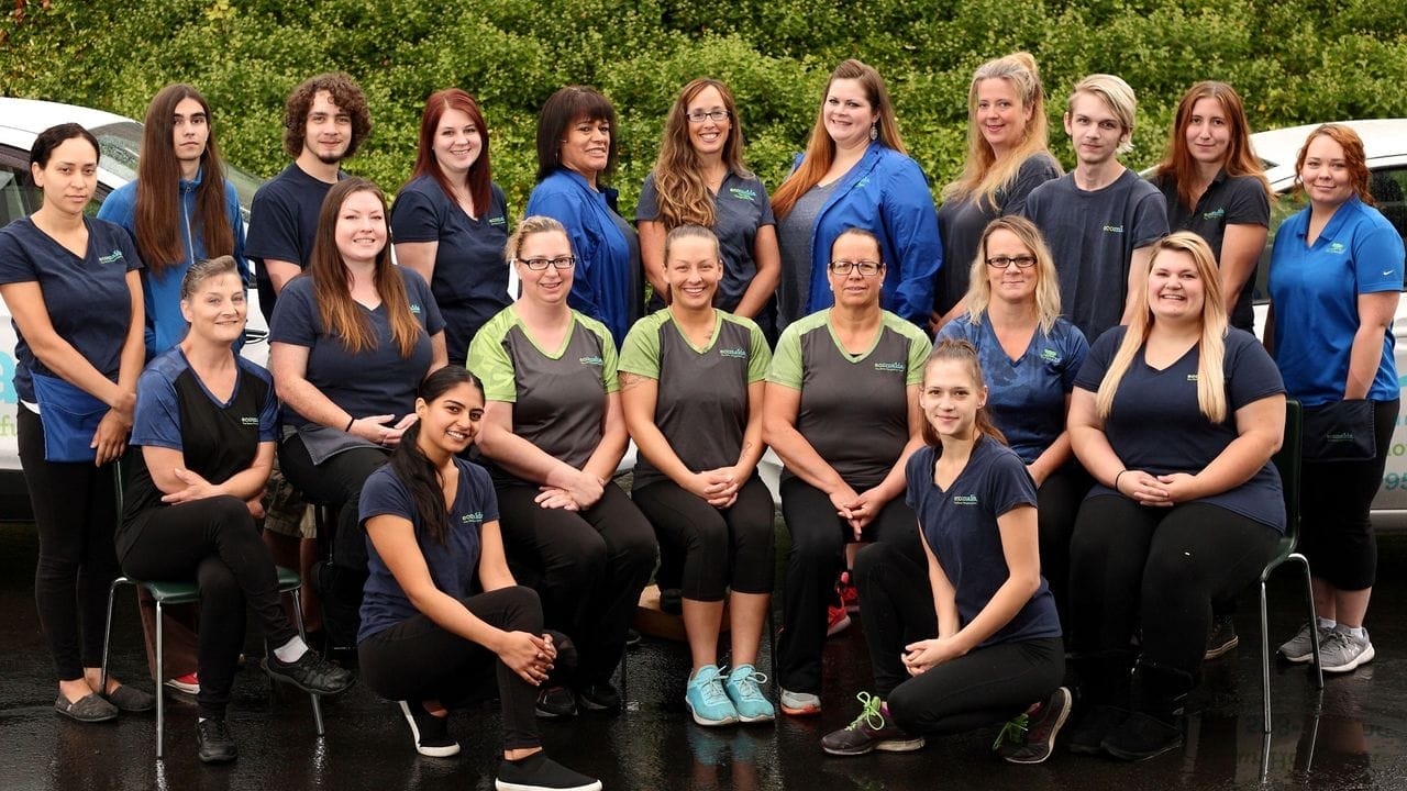 Group of diverse Ecomaids franchise members, in uniform, posing for a photo outdoors.