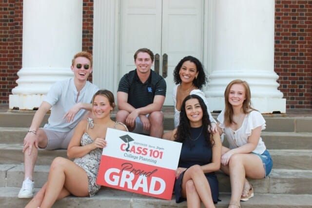 A group of smiling young adults posing with a sign that says "proud grad" celebrating their completion from the Class 101 franchise program.