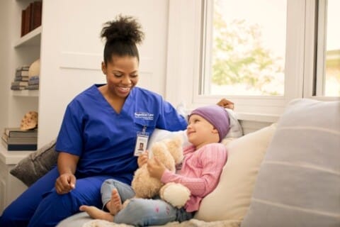 Healthcare professional from BrightStar Care smiling at a young patient holding a teddy bear.