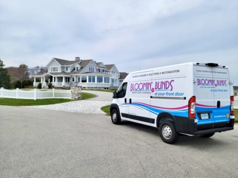A Bloomin' Blinds franchisee service van parked near a large house with a driveway.