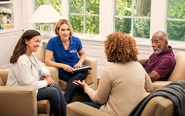 Four individuals in a casual meeting, with two healthcare professionals from BrightStar Care franchise engaging in a discussion with a couple in a bright room.