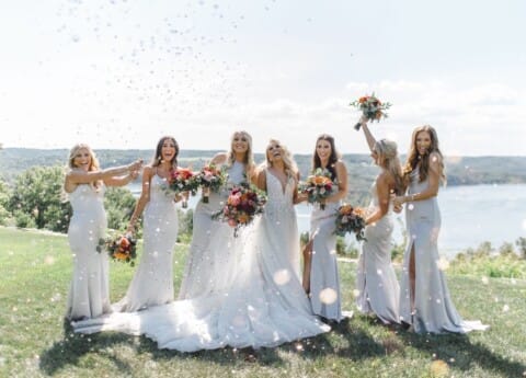 Bridal party celebrating with confetti outdoors on a sunny day.