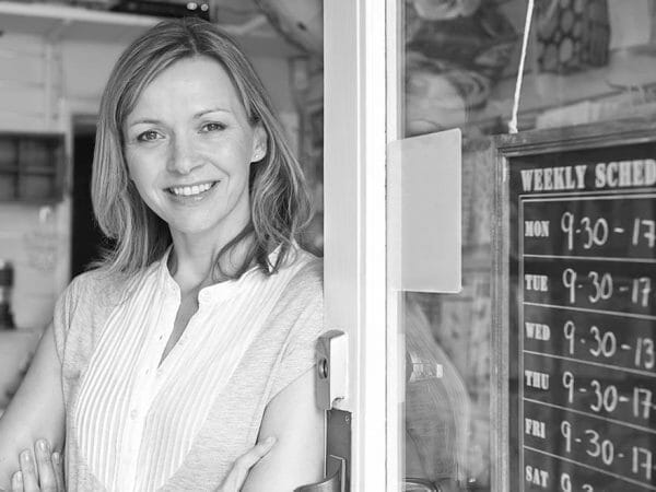 A smiling franchisee standing at the entrance of a shop next to a weekly schedule sign.