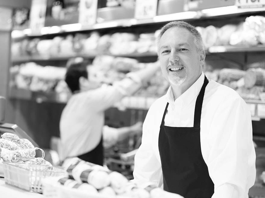A smiling franchisee in an apron standing in front of the bakery section of a grocery store.