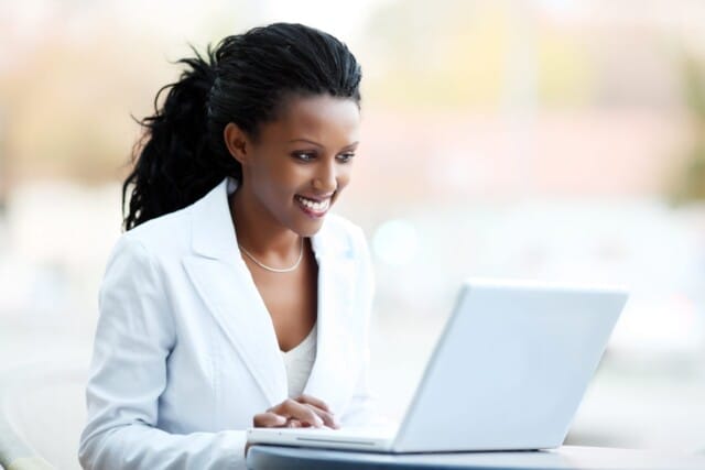 Professional woman working on a laptop with a smile as a franchisee for Assisted Living Locators.