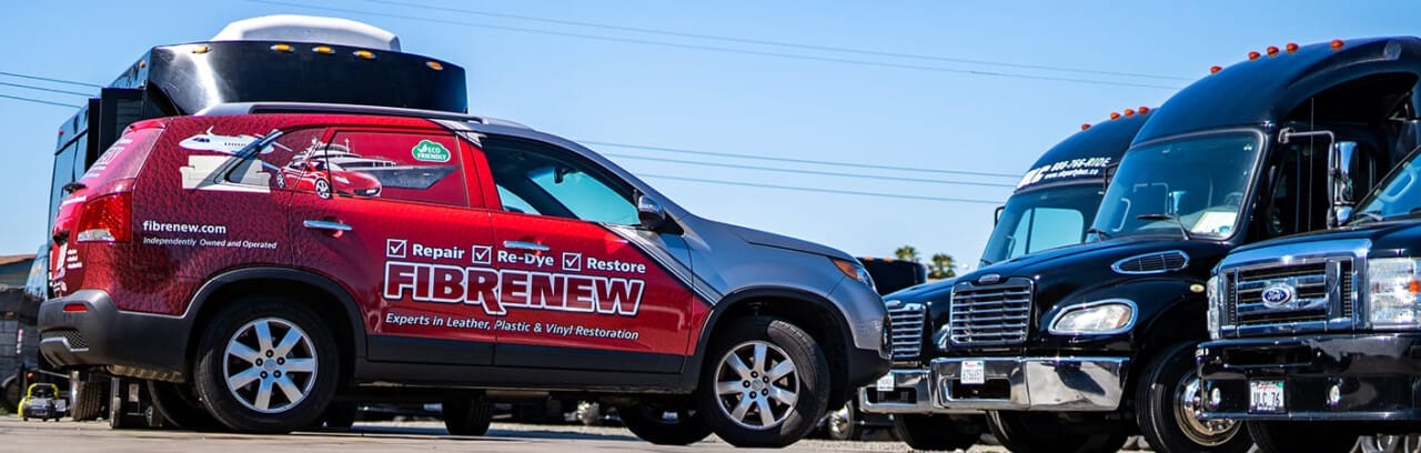 A red Fibrenew vehicle with company branding is parked next to a black truck under a clear blue sky.