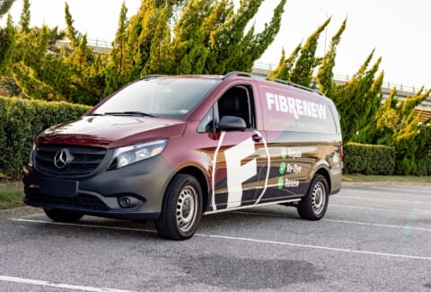 A maroon Mercedes-Benz van with "FIBRENEW" branding is parked in a parking lot, with trees and a building in the background.