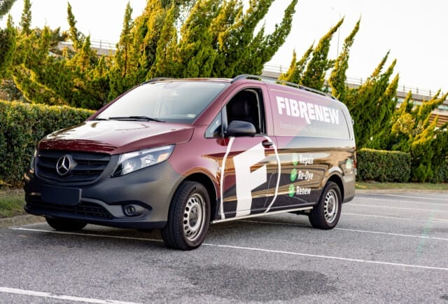 A maroon Mercedes-Benz van with "FIBRENEW" branding is parked in a parking lot, with trees and a building in the background.