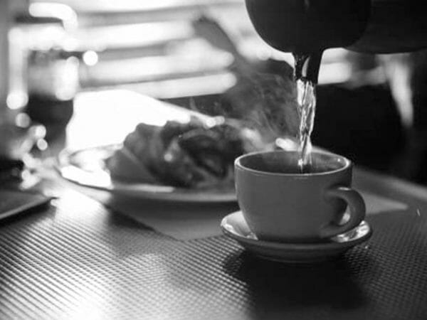 Pouring hot coffee into cup on a table, in a franchise coffee shop with a blurred background.