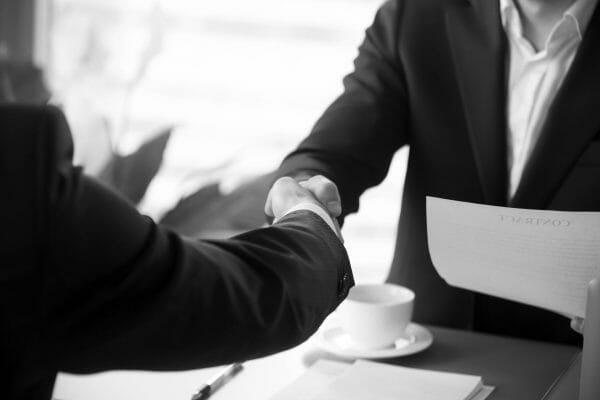 Two individuals shaking hands over selling a franchise agreement.