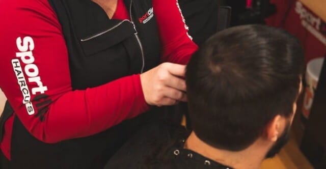 A stylist in a red and black uniform is expertly delivering fresh haircuts at Sport Clips.